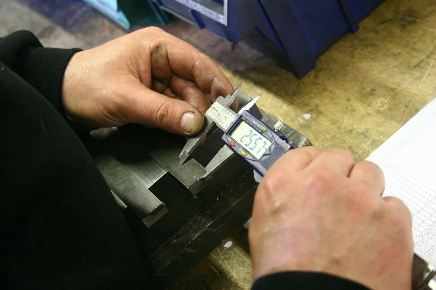 Hands measuring a machined metal part with a digital caliper